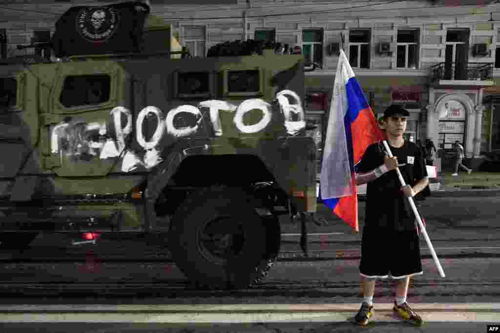Мужчина держит российский национальный флаг перед автомобилем ЧВК «Вагнер» с надписью «Ростов»