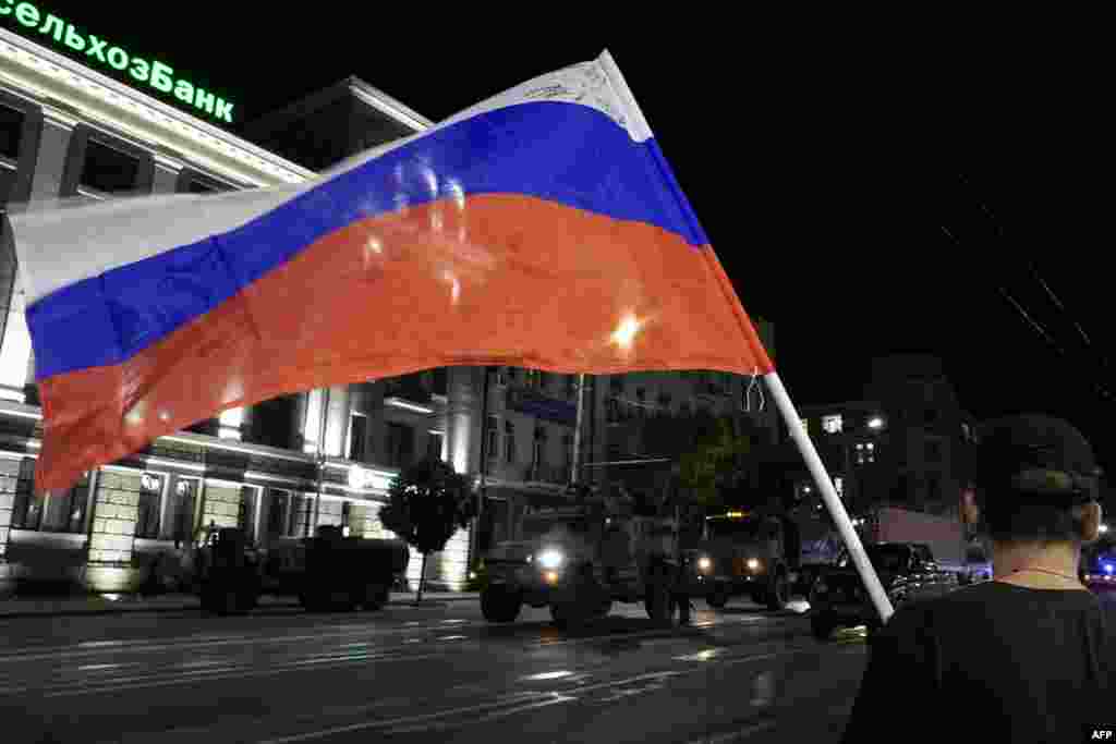 Мужчина машет российским флагом на фоне машин членов группы "Вагнер", покидающих штаб Южного военного округа в Ростове-на-Дону, вечер 24 июня