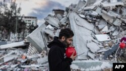 Огун Север Окур, 38-летний турок, надувает красные шары на обломках рухнувшего здания в Антакье — это «последние игрушки» детей, погибших во время землетрясения, разрушившего этот южный турецкий город