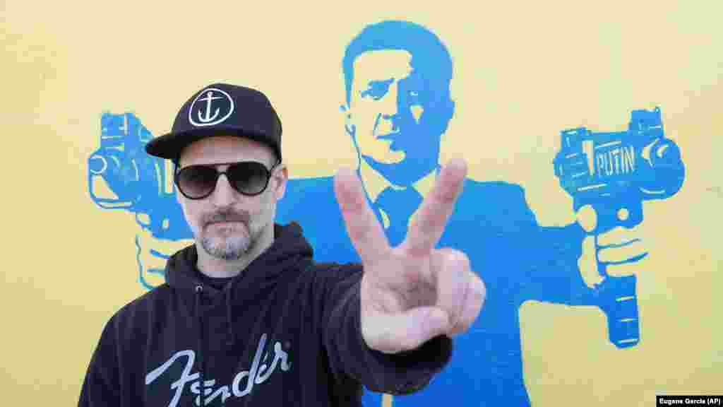 Вуличний художник Тодд Гудман, відомий як 1GoodHombre, стоїть перед зображенням президента України Володимира Зеленського. автоматами в руках, Санта-Моніка, Каліфорнія, 21 березня 2022 року. Гудман відмовився від анонімності, ризикуючи арештом та штрафами за неліцензовану роботу зі збору коштів для українських біженців. Гудман сказав Радіо Свобода, що його роботи – заява про мирний ненасильницький опір неконтрольованій агресії та насильству Путіна в Україні. «Я гадки не маю, чи може моя робота фізично щось змінити, окрім, можливо, зміни почуття безнадійності та страху на почуття надії та хоробрості перед лицем зла»